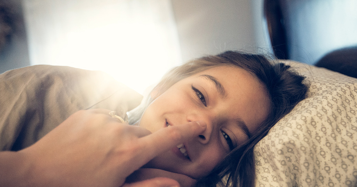 Mädchen liegt Betrachter gegenüber, wird an der Nase berührt und lächelt.