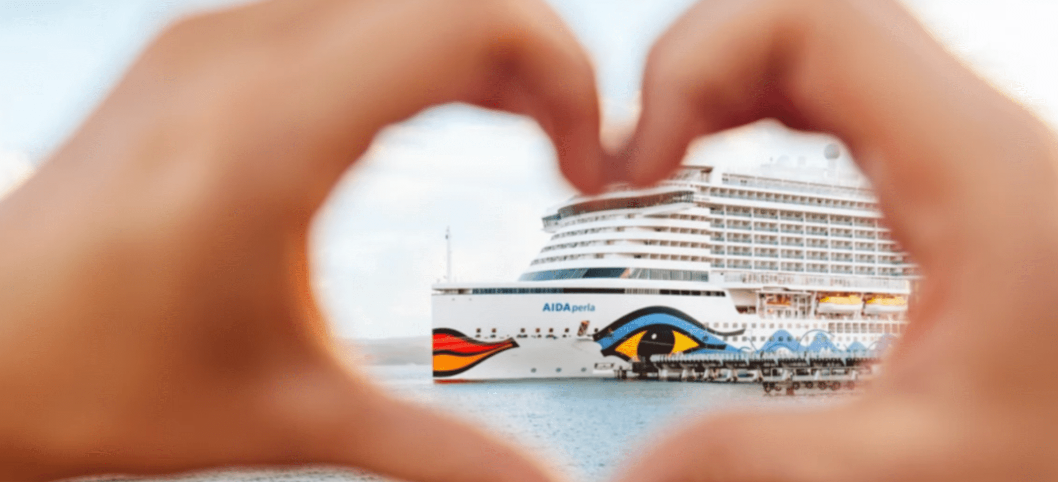 Zwei Hände formen ein Herz vor einem AIDA Kreuzfahrtschiff
