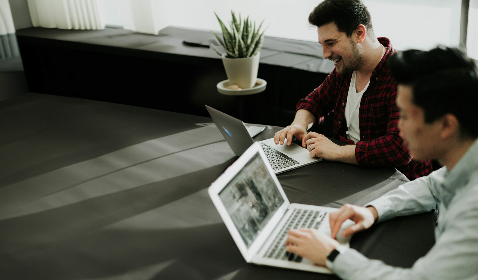 Zwei Kollegen arbeiten gemeinsam an Laptops in einem Besprechungsraum.