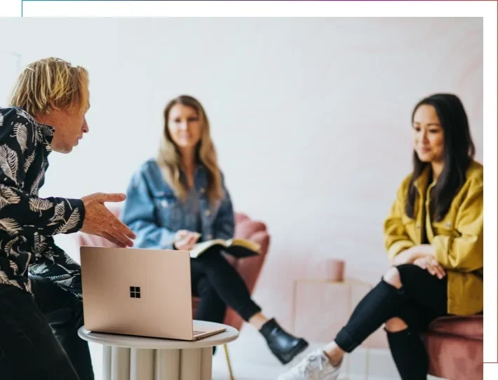 Ein Mann zeigt zwei Frauen etwas am Laptop.